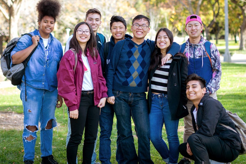A group of eight male and female students representing a mixture of ethnicities smile for a picture.